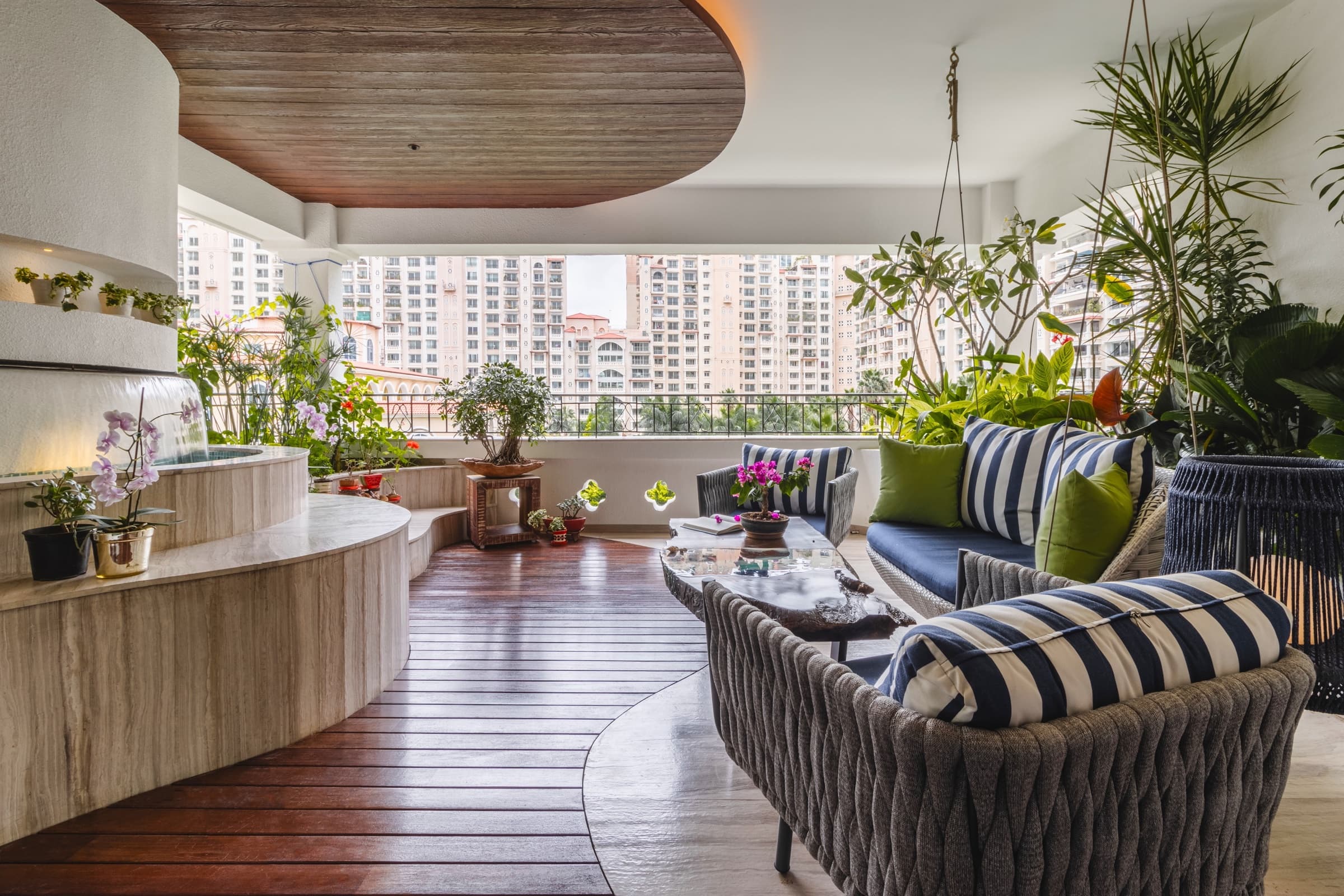 A sunlit balcony with curved benches, plants, and a treetop city view.